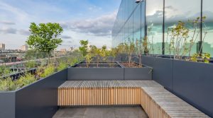 Anthracite metal planters with integrated bench seating on a modern UK rooftop terrace with planting and glass facade