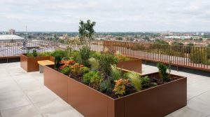 Corten steel metal planters on a UK rooftop terrace with mixed planting, integrated seating and city skyline views