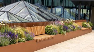 Corten steel planters with integrated timber bench seating and flowering plants on a modern commercial rooftop terrace in the UK