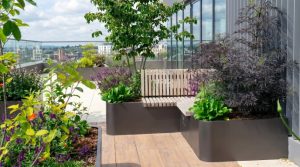 Metal planter with integrated bench seating and lush planting on a modern UK rooftop terrace with timber decking