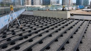 Metal planter roof terrace substructure with black aluminium support rails, adjustable pedestal bases and gravel build-up prepared for a modern urban terrace installation.