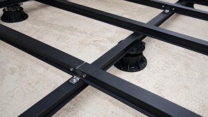 Metal planter subframe detail showing black aluminium rails fixed together with stainless steel bolts and supported by adjustable pedestal bases for a roof terrace system.