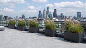 Four-panel installation sequence for roof terrace planters UK roof terrace, showing adjustable pedestals on a flat roof, planter positioning, drainage aggregate with geotextile membrane, and the completed planted terrace system.